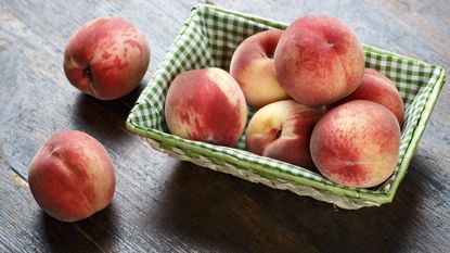 Ripe freshly-harvested peaches in a basket on a wooden background