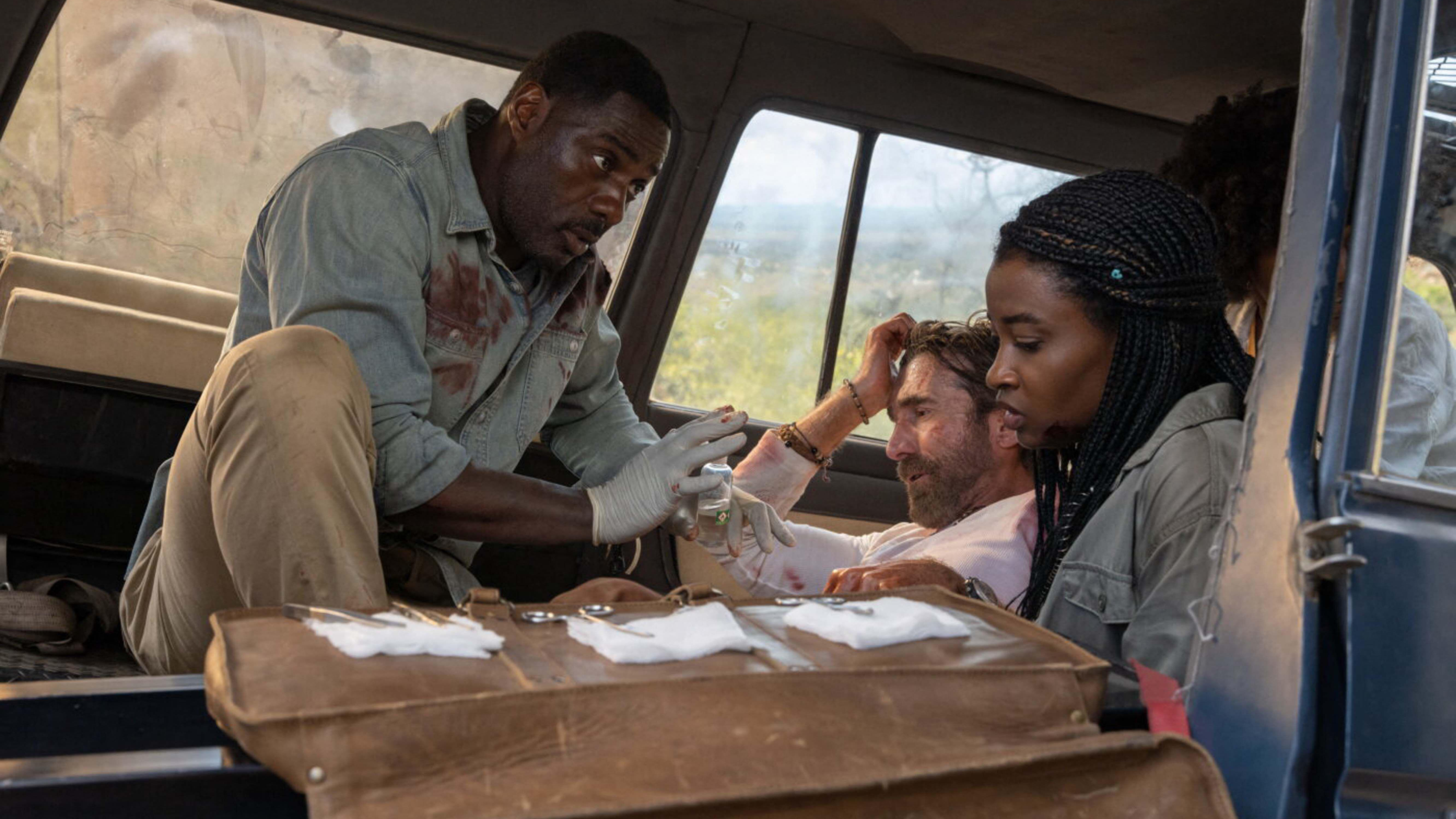 L-R: Dr. Nate Daniels (Idris Elba) attends to a wounded Martin Battles (Sharlto Copley) with the help of his daughter Meredith (Iyana Halley) in a car in a scene from "Beast"