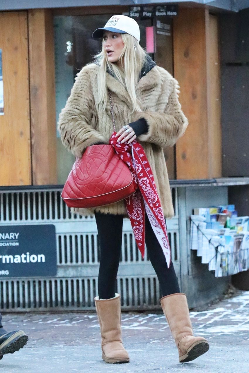 Bella Hadid wearing a fur coat, baseball cap, red triangle scarf, leggings, and Ugg Classic Tall Boots in Aspen