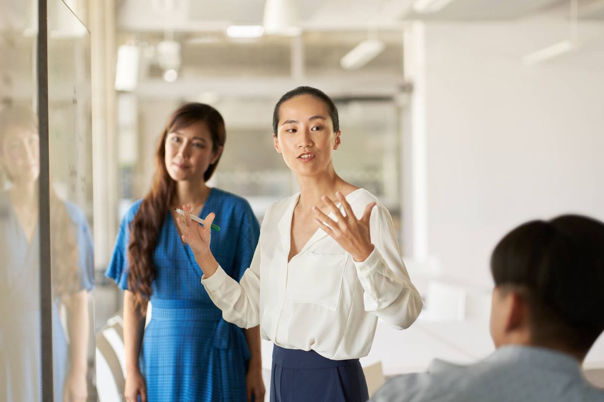 Three colleagues chat in front of a whiteboard covered in written notes