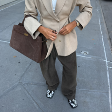 An image of an influencer wearing an alternative to dated autumn shoe trends&mdash;animal print loafers&mdash;with dark grey trousers, a waisted beige blazer and holding a brown suede tote