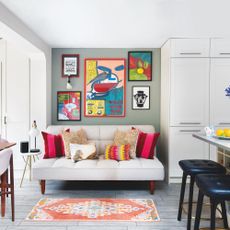 small white sofa in kitchen alcove, with colourful cushions and artworks on wall above, with rug on floor