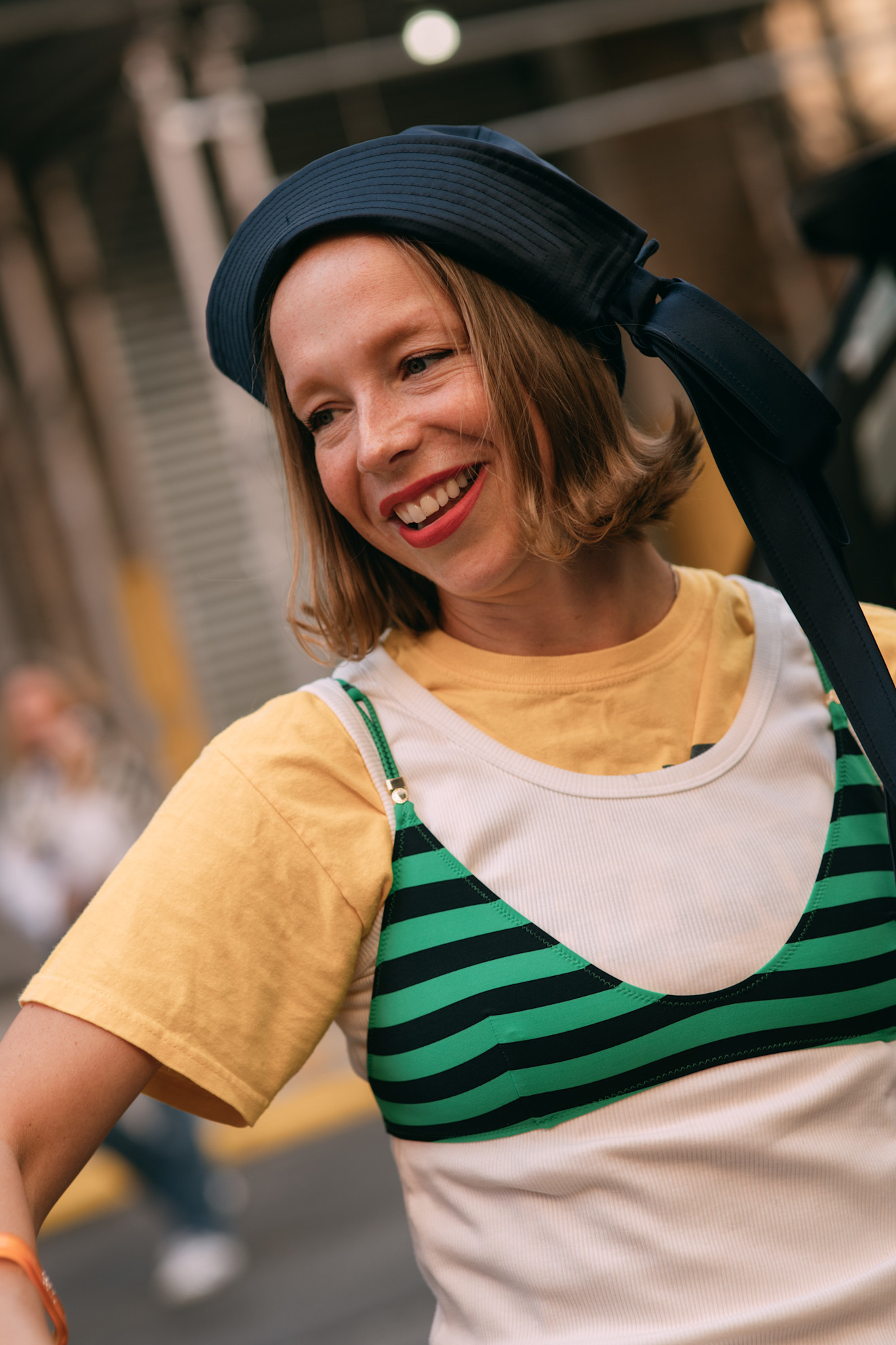 chloe king wears a yellow, white and green t-shirt with a red lip and blonde flippy bob and beret