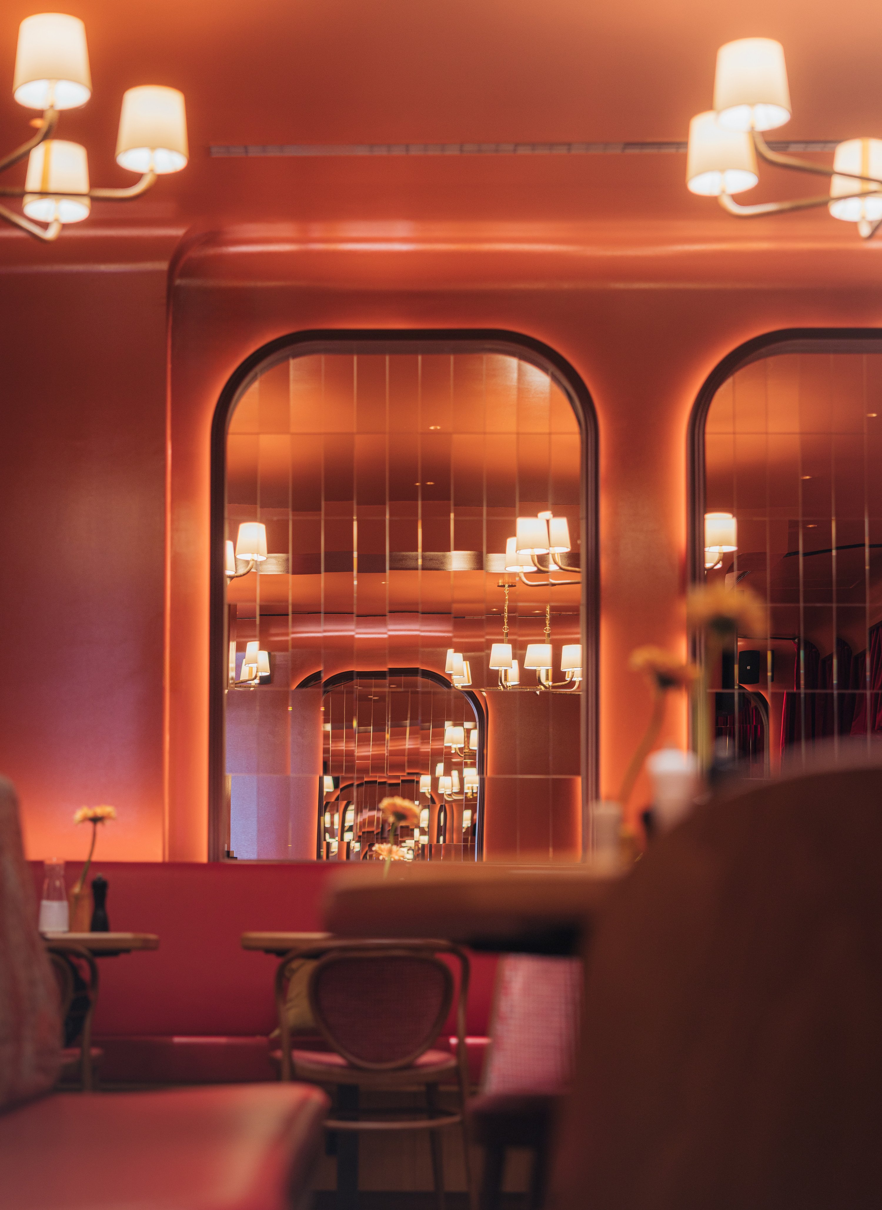 A coral-tinted Art Deco cafe merges 20th-century and contemporary style through plush fabrics, softly glowing chandeliers, fragmented, round-eyed mirrors, leathery sits, and atmospheric flair.