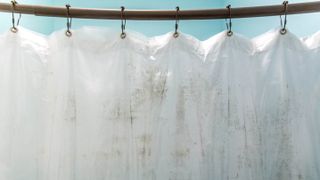 The rings and top section of a white shower curtain which is stained