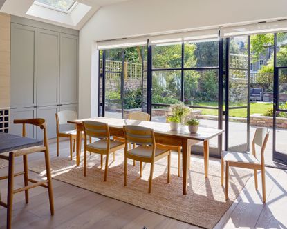 An example of kitchen extension ideas showing a kitchen with a large wooden dining table with chairs in front of glass doors with black frames