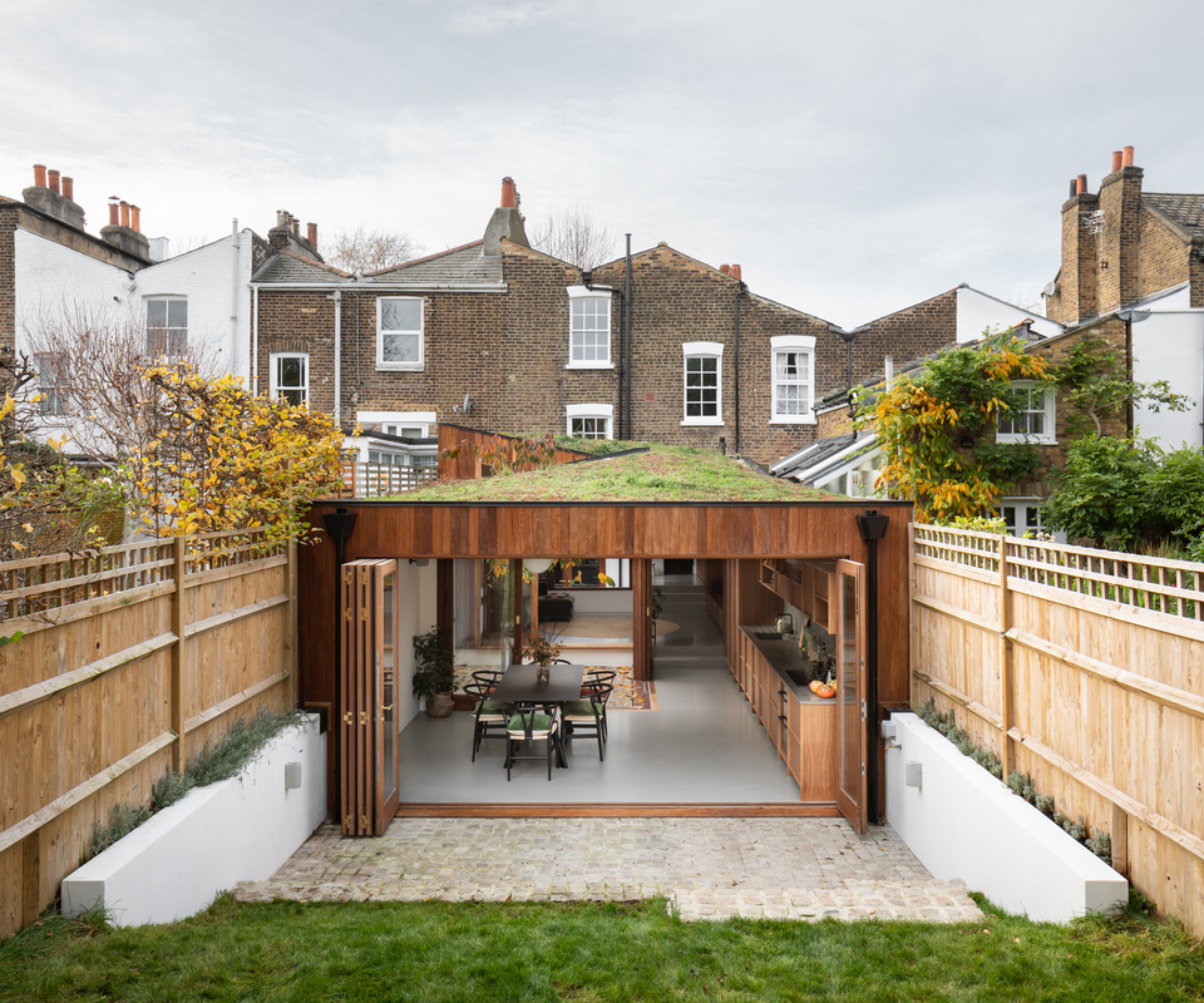 single storey extension running along length of garden with green roof and large wooden bi-fold doors at end leading onto patio and lawn