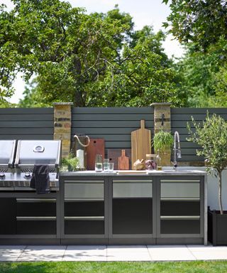 Outdoor kitchen in linear layout with mixed wooden chopping boards stacked on countertop.