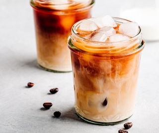 A cup of iced coffee with coffee beans scattered around it