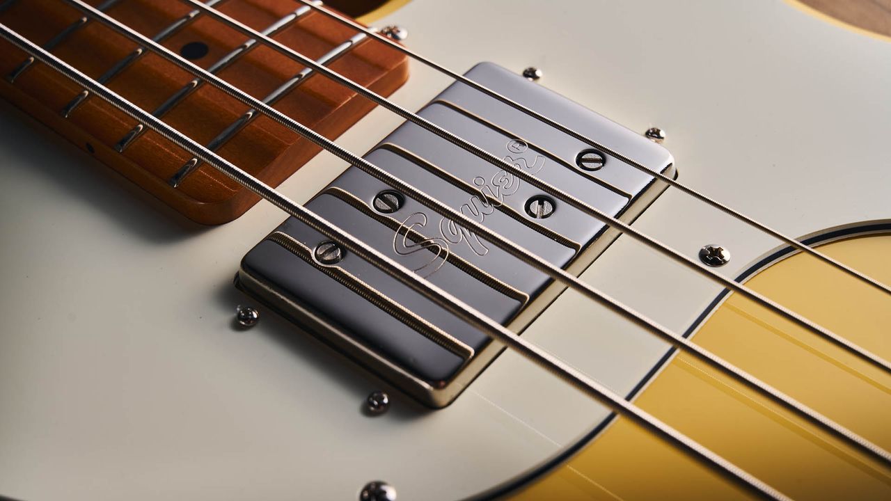 The Squier Classic Vibe Telecaster Bass is a fine-looking four-string in a custard-colored Vintage White, and is here photographed in close-up, against a plain wooden background. It has a single Wide Range humbucker.