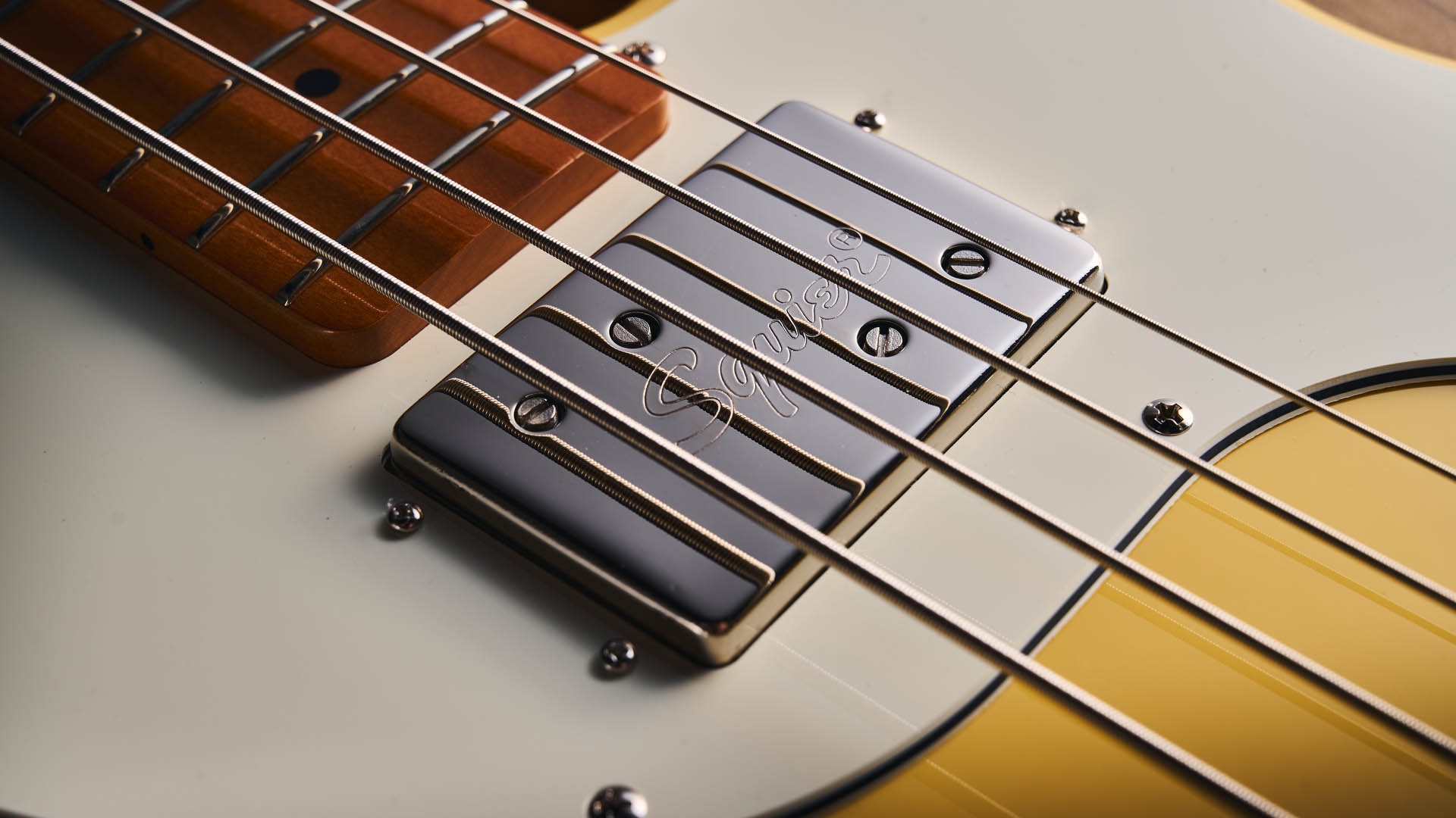 The Squier Classic Vibe Telecaster Bass is a fine-looking four-string in a custard-colored Vintage White, and is here photographed in close-up, against a plain wooden background. It has a single Wide Range humbucker.