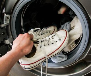 A pair of white sneakers being put into a washing machine