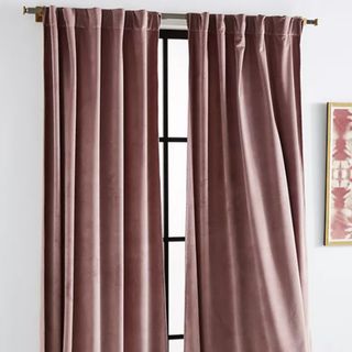 Pink crushed velvet curtains hung on a curtain rail in a window. 