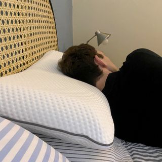 A man with dark hair laying on the Emma Premium pillow. His back is to the camera and he's laid on a bed with a grey and white striped duvet cover