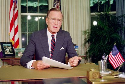 Then-President George H.W. Bush poses for photographers after his address to the nation, 27 September 1991, in the Oval Office of the White House. 