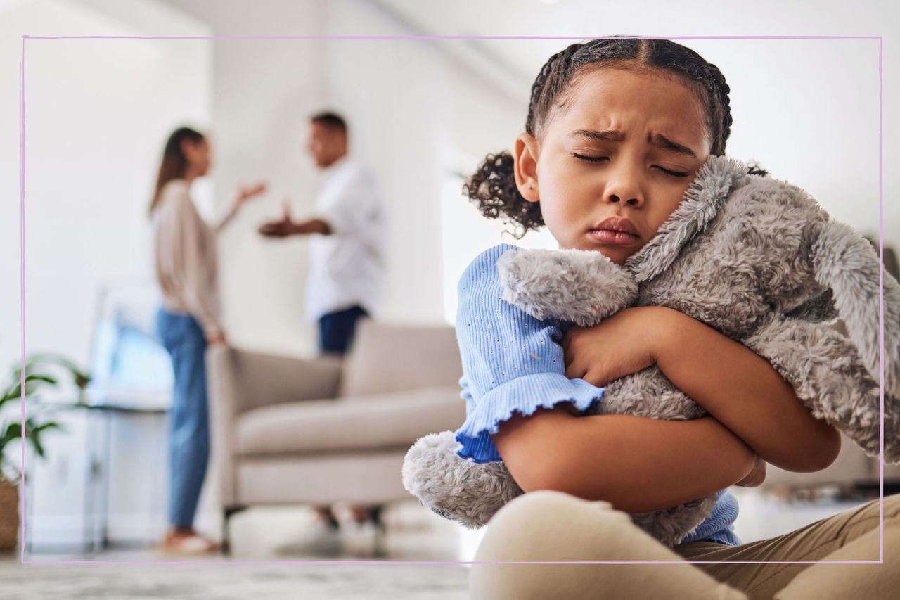 Sad girl hugging a soft toy while parents argue behind her