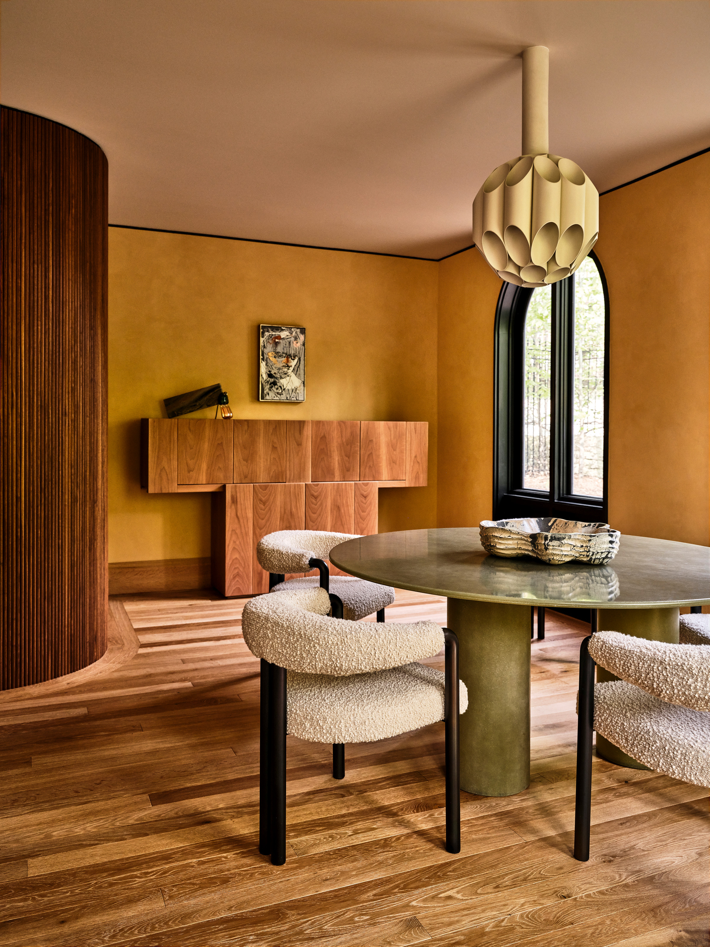 Ochre dining room with textured walls, wood floor, wood credenza, green round dining table and boucle chairs