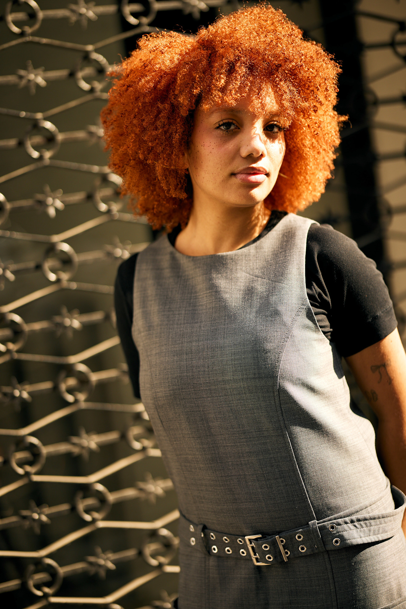 a black woman with a red afro wearing a gray dress with a silver belt