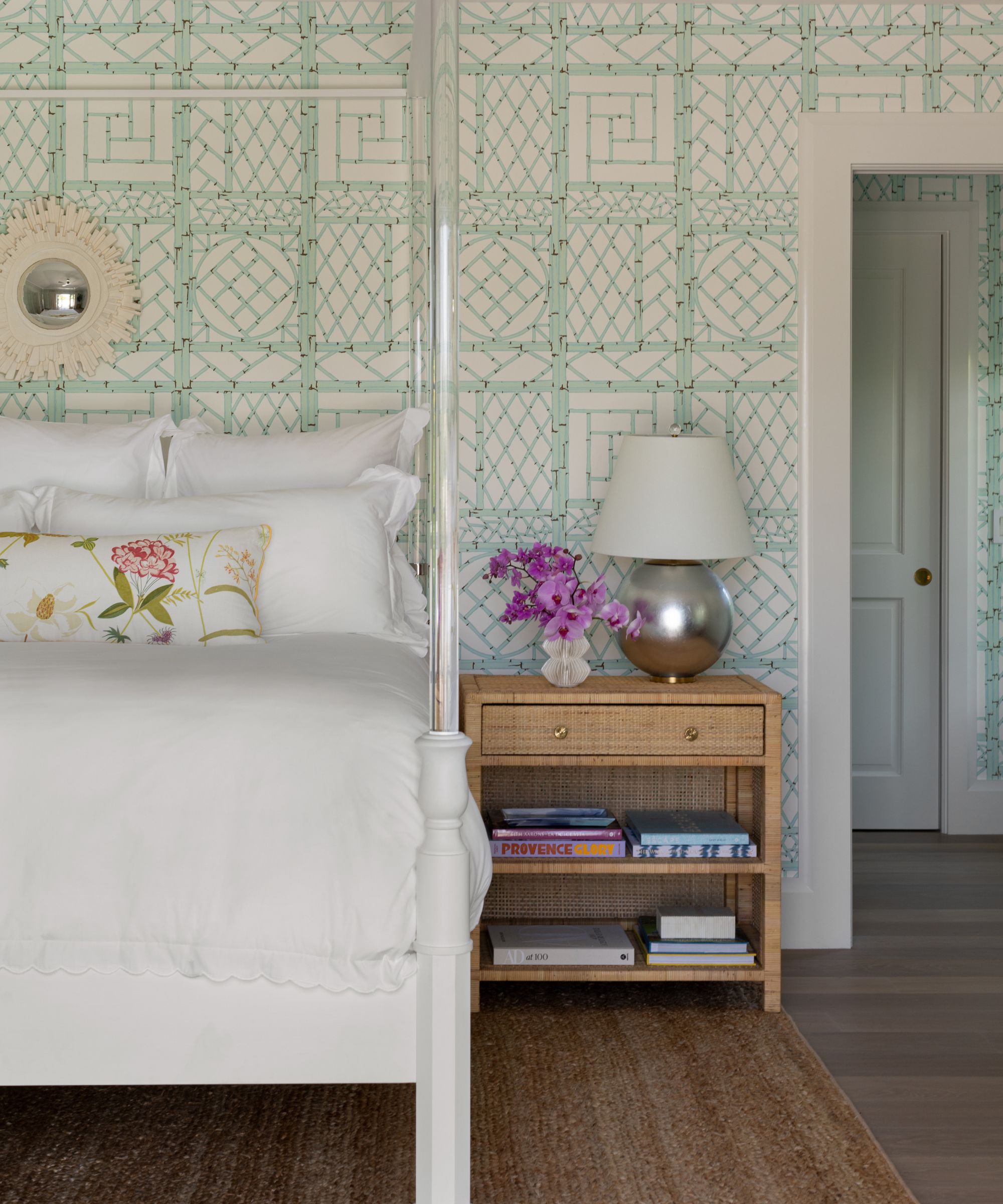 A bedroom with mint green wallpaper, a bed with white bedding, a wooden nightstand, and a jute rug.