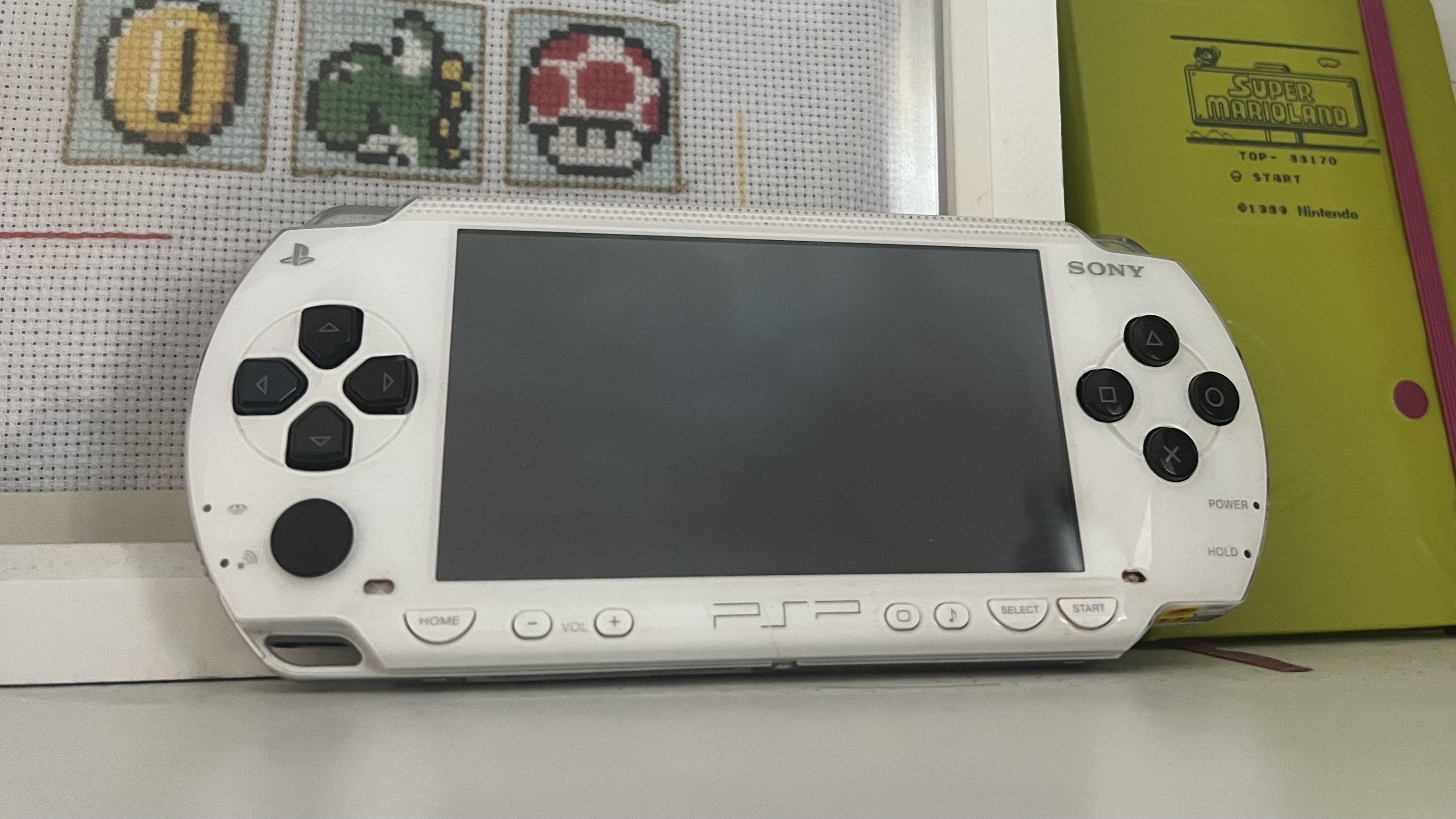 White PSP handheld on a shelf with a Nintendo-themed picture and notebook