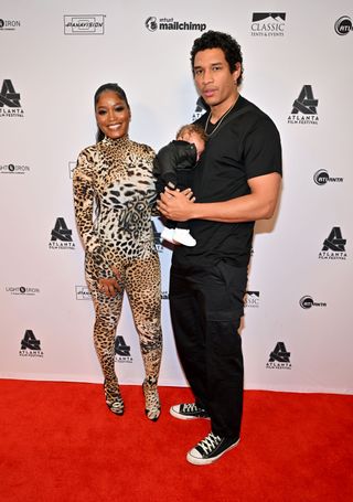 Keke Palmer in a leopard catsuit standing on the red carpet with Darius Jackson, who is holding their baby Leo