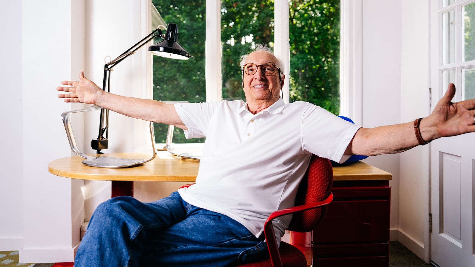 man smiling, with arms wide open, sitting in red office chair