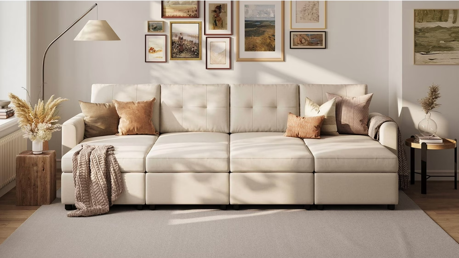 a living room with a large cream couch with pillows on it, a gallery wall on the wall behind, and two small side tables on either side of the couch