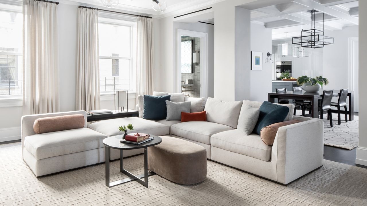 A living room with large, low corner sofa in pale grey and a partially open plan layout leading into a dining room