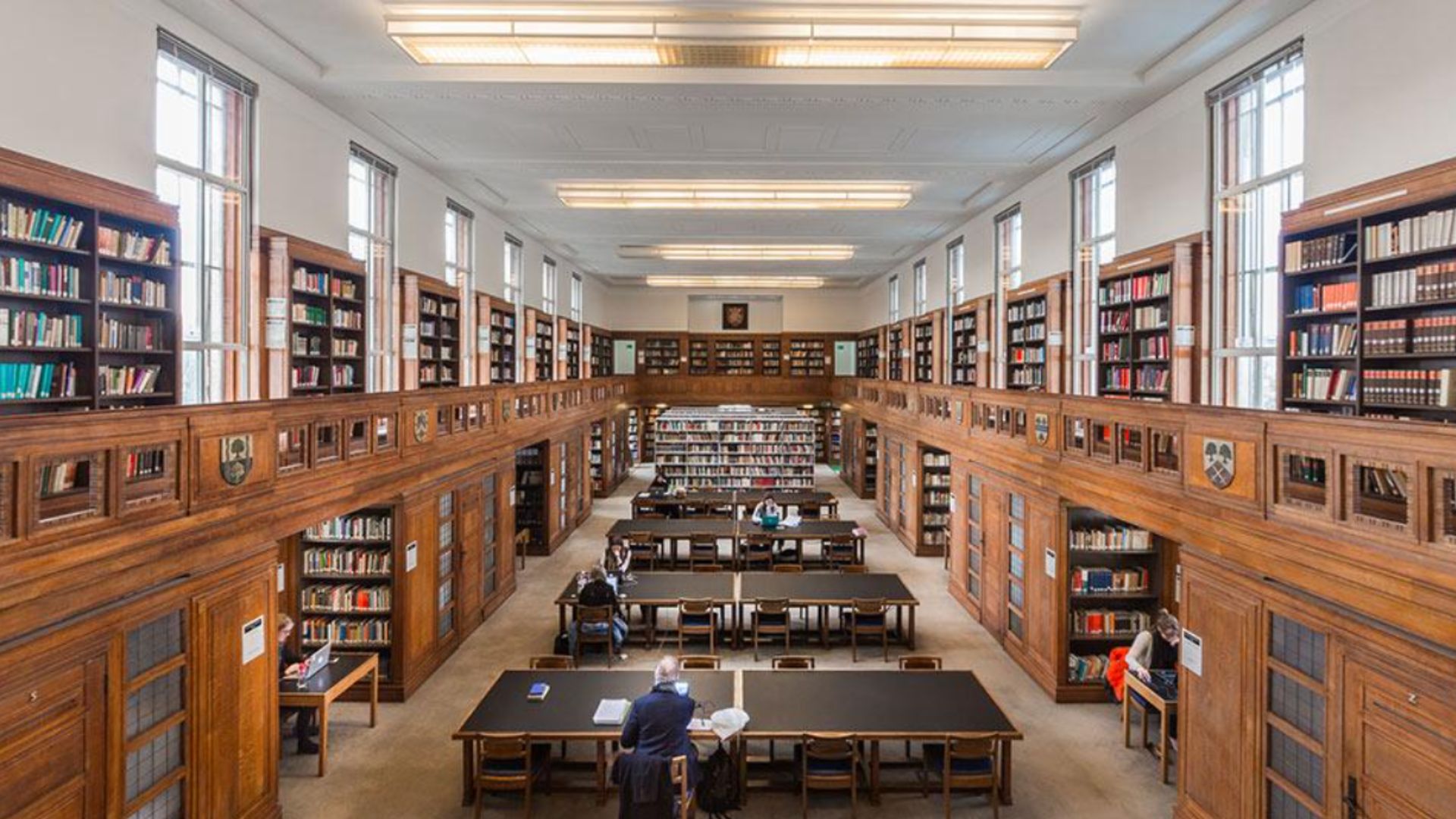 an image of the interior of the senate house library with wooden bookshelves lining two floors with a row of communal tables down the middle