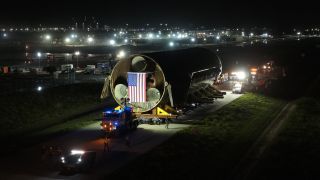 a giant black-tiled rocket lays horizondal as it is transported down a road at night.