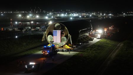 a giant black-tiled rocket lays horizondal as it is transported down a road at night.
