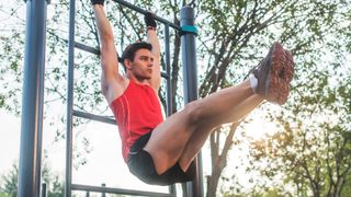 Man doing hanging leg raises from a pole in a park outdoors