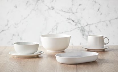 White ceramic tableware including two cups and saucers, a bowl and a narrow plate