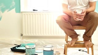 Person sat on stool in a room being painted with painting tools on floor