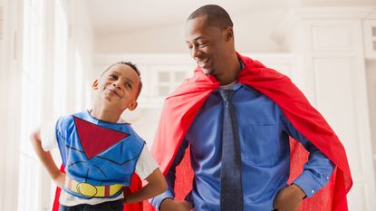 A smiling father and son where super hero capes.