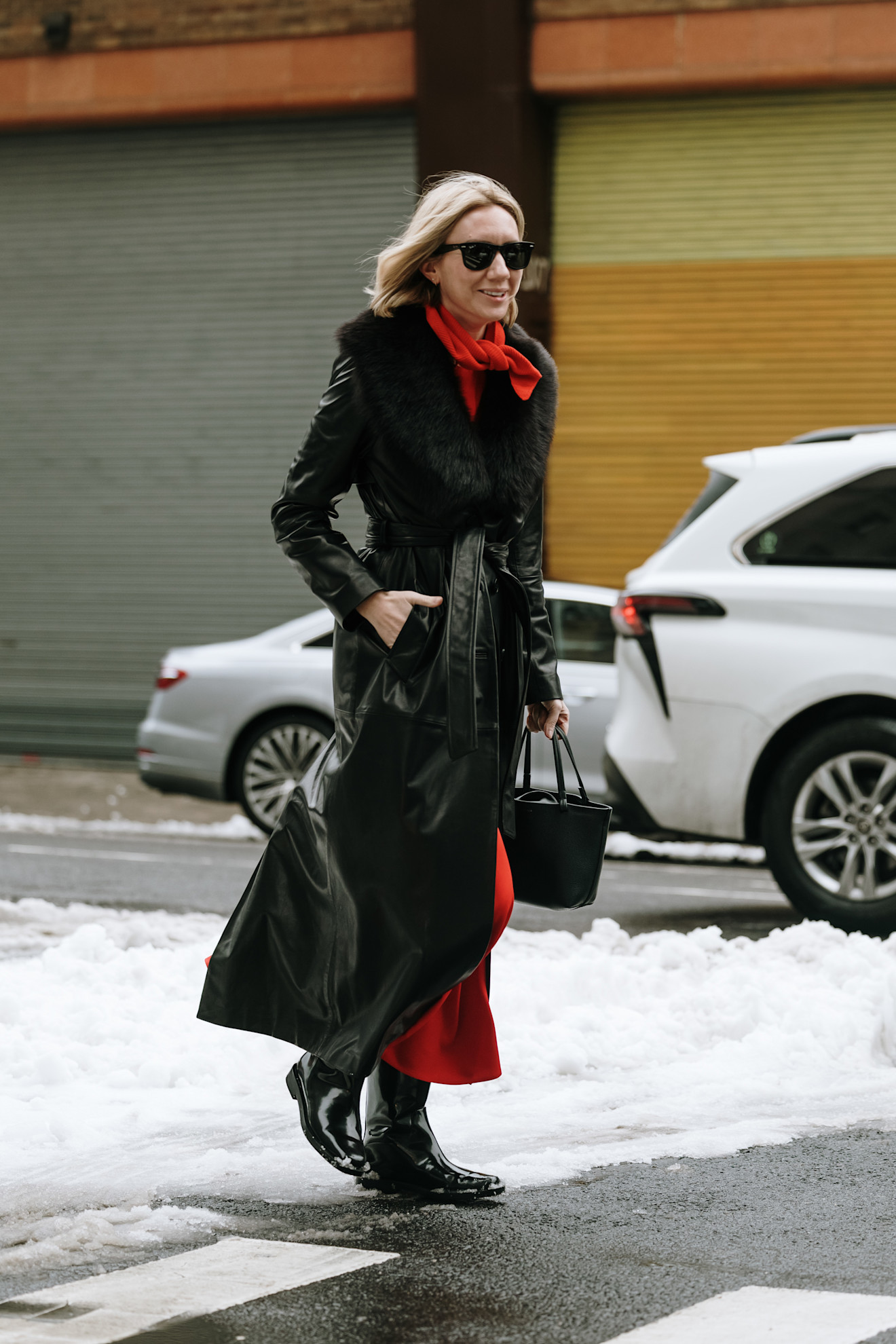 a woman at new york fashion week wearing a red triangle scarf, black fur trim jacket, a red dress, and black boots