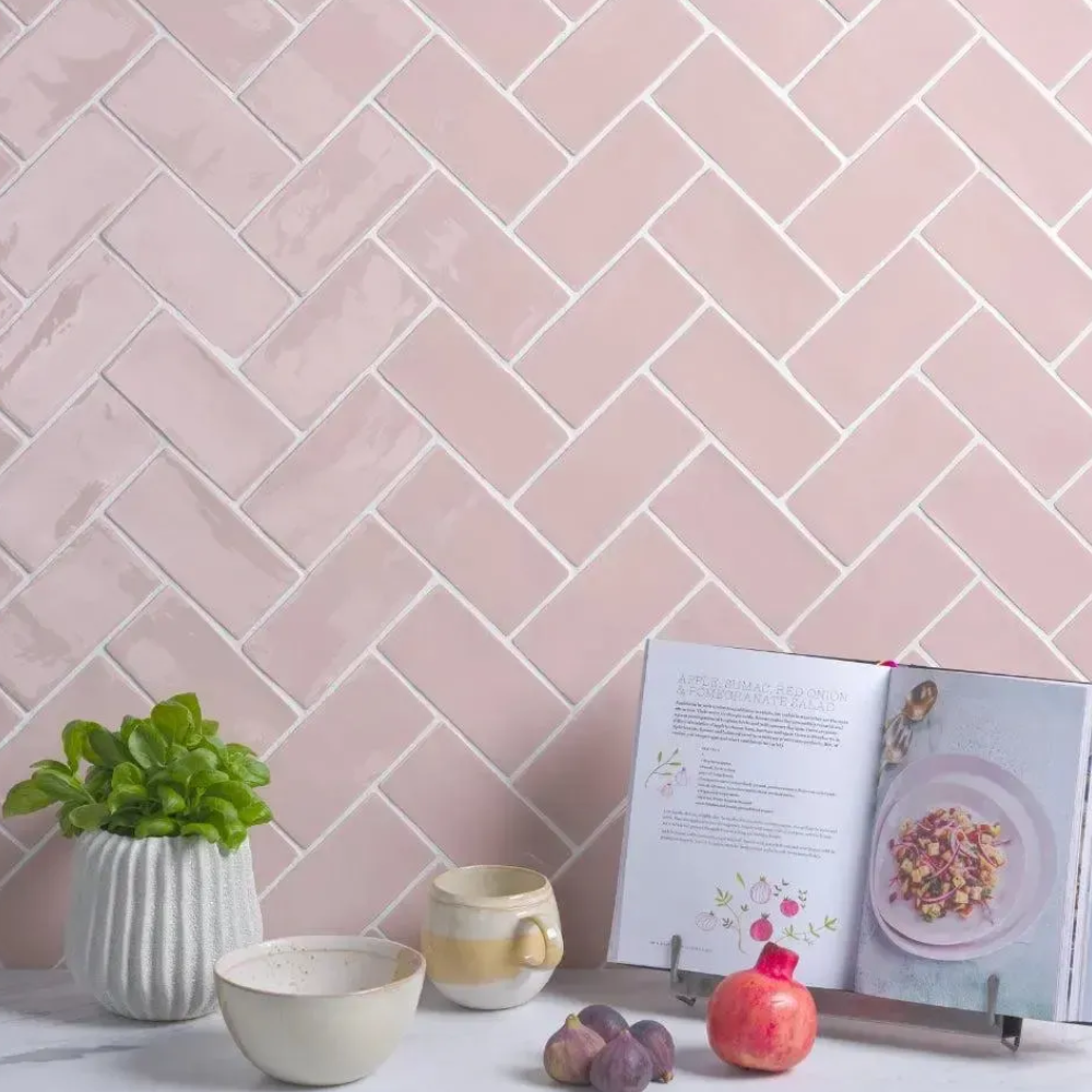Pink tiles with kitchen accessories and food on worktop in front