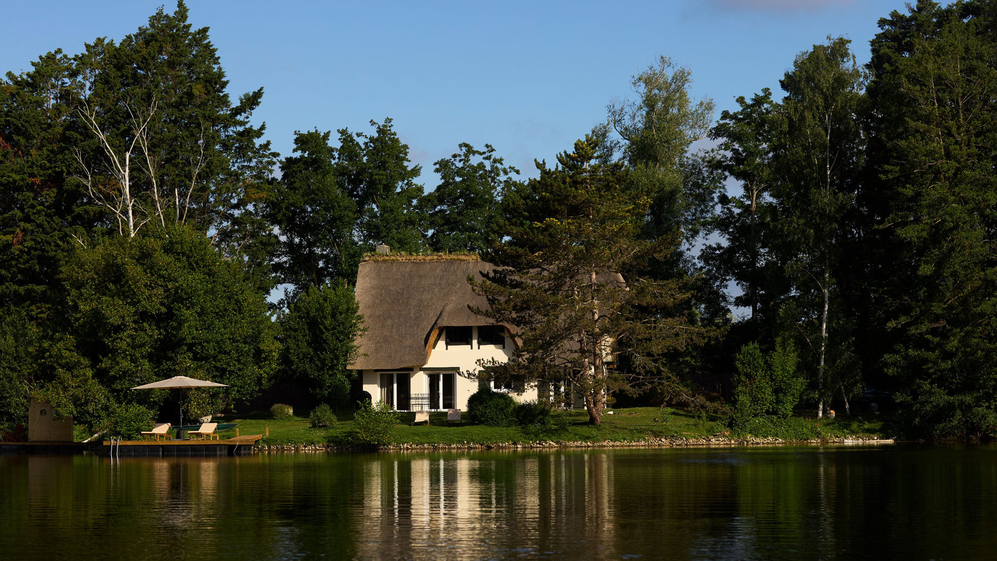 a striking exterior shot of a thatched cottage by a lake in France