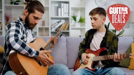Man with acoustic guitar and young man with electric guitar sit on a grey sofa