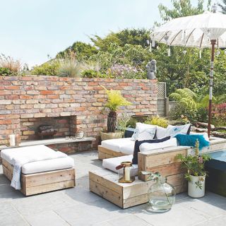 garden with pallet furniture with cushions and a brick wall with fire pit