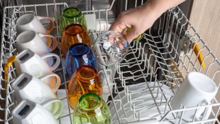 A dishwasher upper basket filled with mugs and colorful glassware