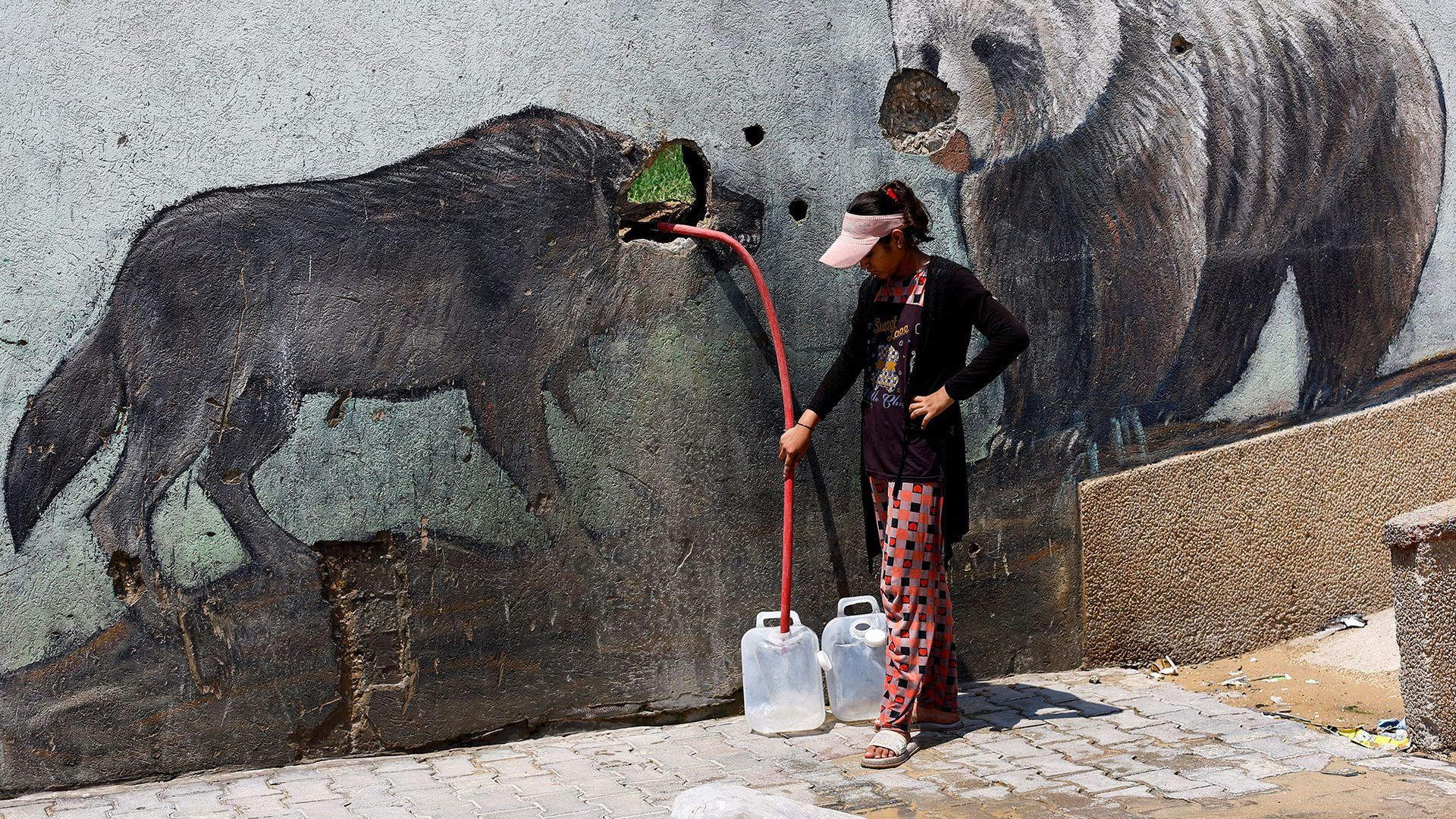 
                                A Palestinian girl fills water containers outside the wall of a zoo damaged by Israeli attacks, in Gaza City, Palestine
                            