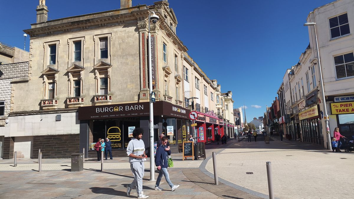 This picture shows a bustling town center street lined with buildings housing a Burger Barn and other businesses.