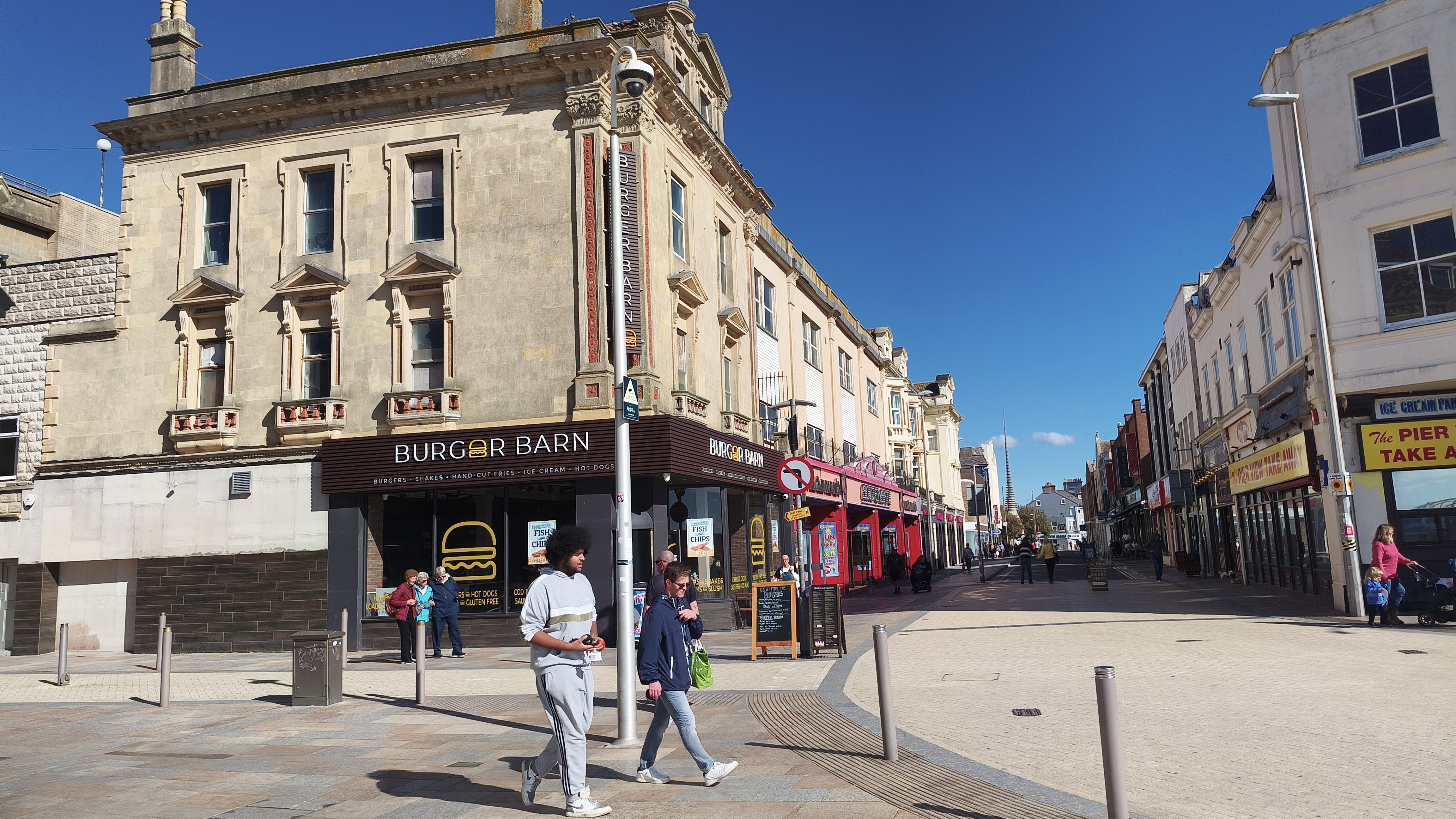 This picture shows a bustling town center street lined with buildings housing a Burger Barn and other businesses.