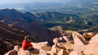 A hiker sits on a pile of boulders on Pikes Peak overlooking colorado