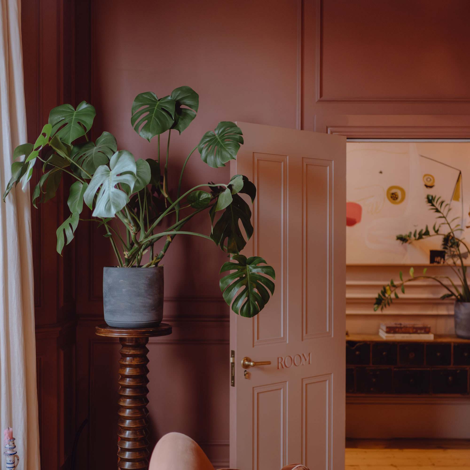 Red living room with pale pink door and a monstera plant
