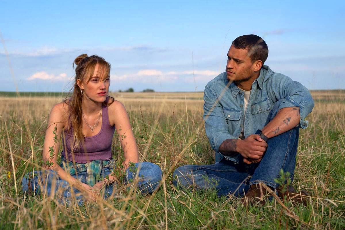 maika monroe as kenna and tyriq withers as ledger sitting in a field together under a sunsetting sky in a still from the romance movie reminders of him