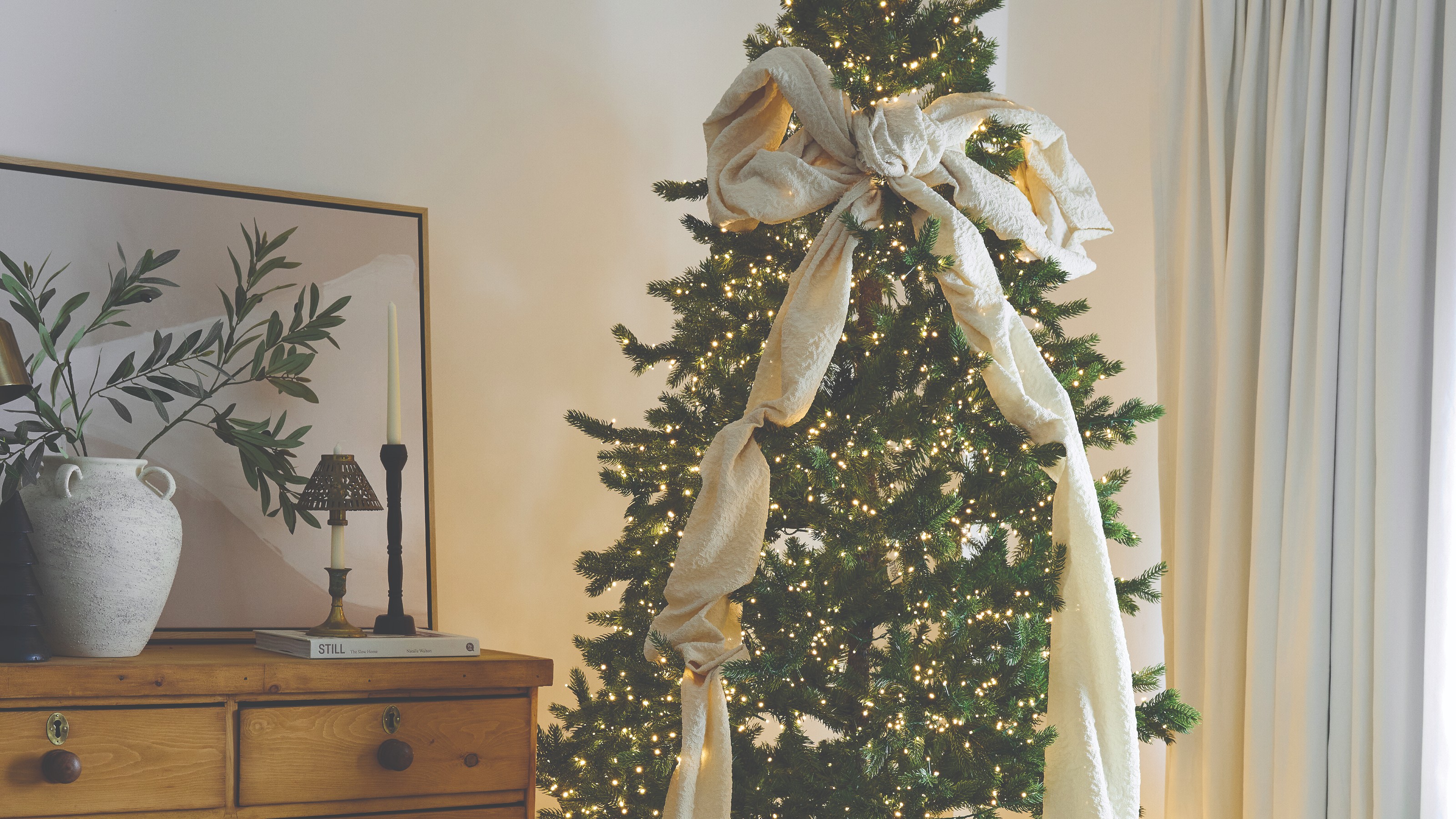 A bedroom with a lit-up Christmas tree decorated with a large off-white bow