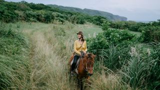 Woman riding horse through grassy tree area