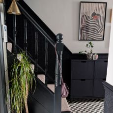 Hallway with lower half of walls painted blue-black, and top half white. Matching blue-black banisters. Black and white chequered flooring